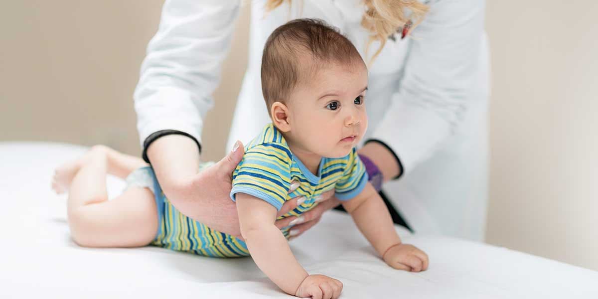 A practitioner gently supports an infant on an examination table, illustrating chiropractic care techniques designed to treat infant torticollis.